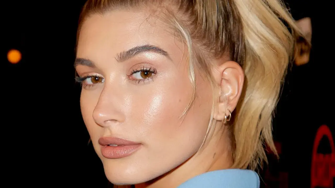 Primer plano de una mujer con piel de cristal, ojos marrones y cabello rubio recogido.