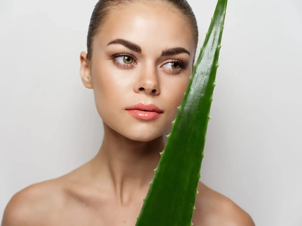 Mujer con piel radiante sostiene una hoja de aloe vera, demostrando que se puede usar aloe vera directamente de la planta para un cuidado natural.