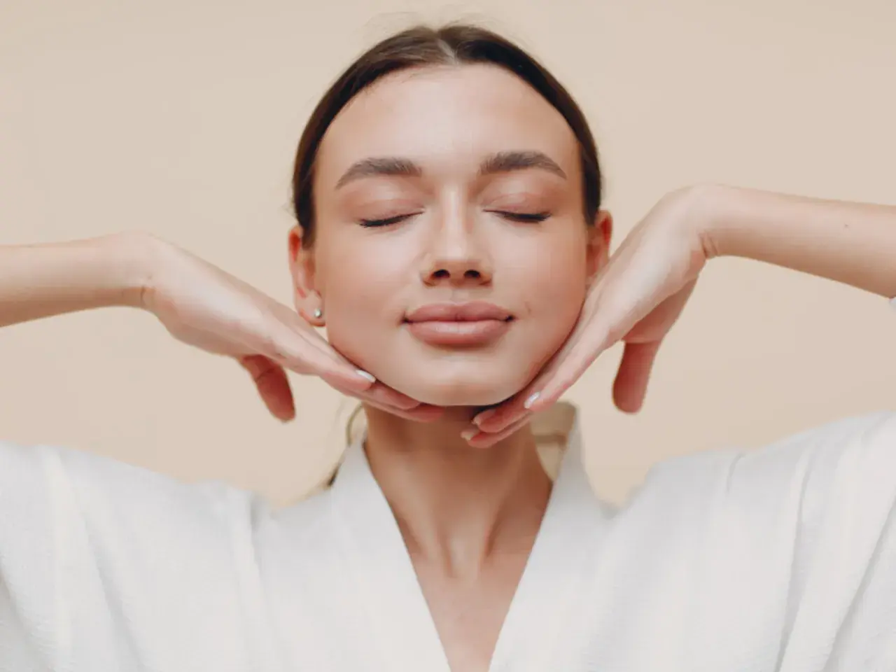 Mujer con ojos cerrados, disfrutando de un masaje facial. Sus manos sostienen suavemente su rostro, practicando yoga facial para una piel radiante.
