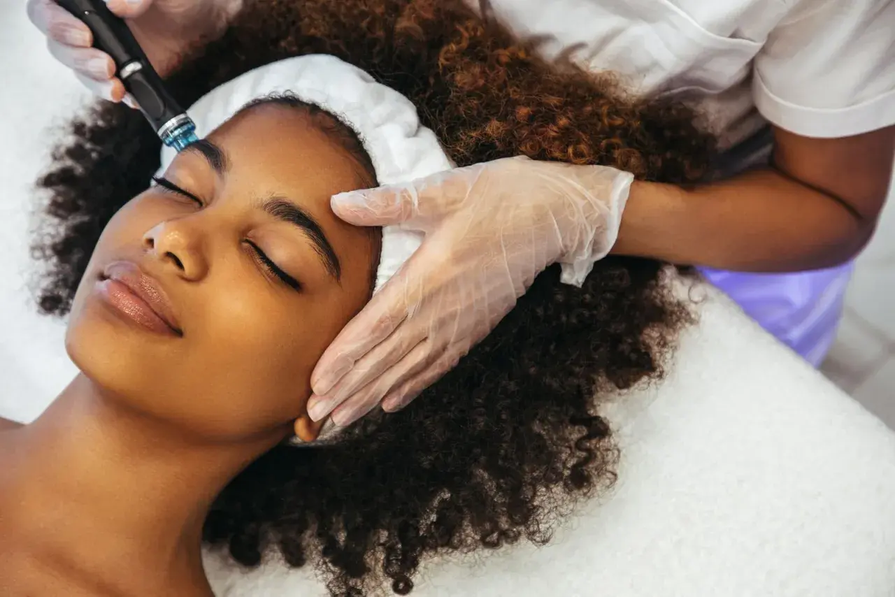 Una mujer disfruta de un tratamiento Hydrafacial. Un profesional con guantes aplica el dispositivo en su rostro para una piel radiante.