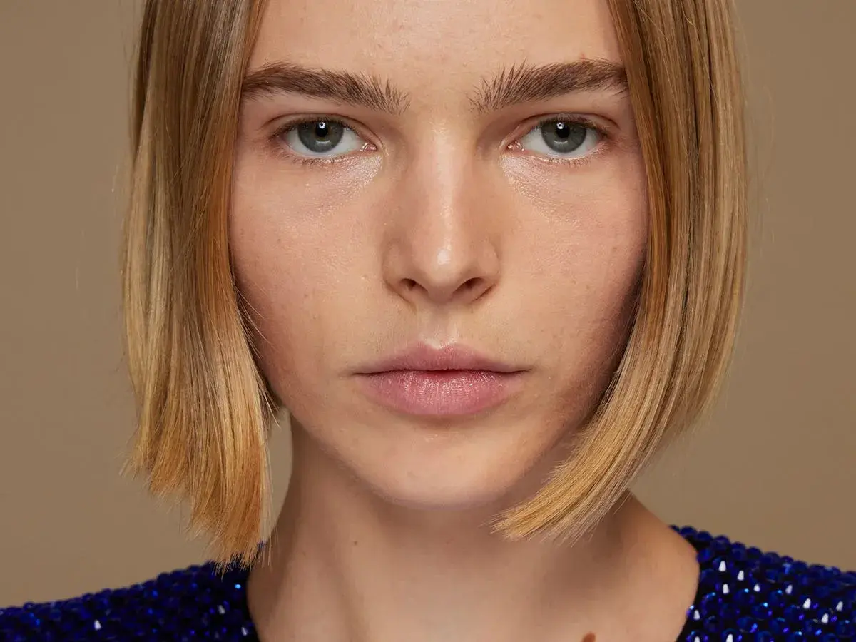 Primer plano de una mujer con un elegante bob peinado, ojos penetrantes y un vestido azul brillante.