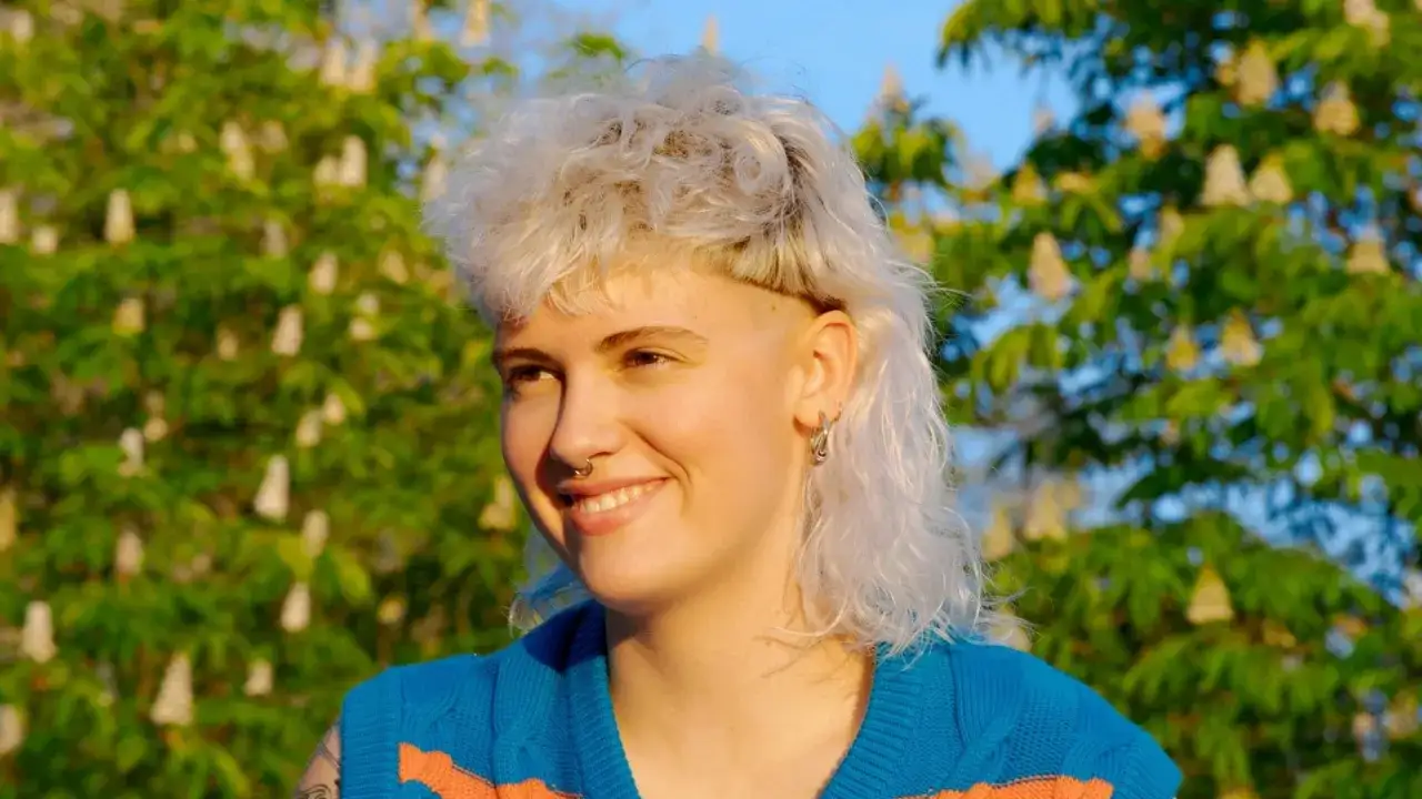 Joven sonriente con un corte de pelo mullet hombre, con el pelo rubio desordenado y rapado a los lados.