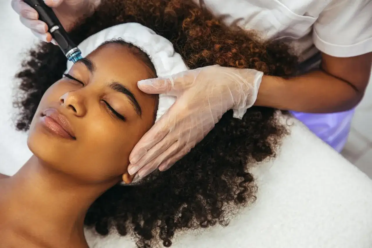 Una mujer disfruta de un tratamiento Hydrafacial. Un profesional con guantes aplica el dispositivo en su rostro para una piel radiante.