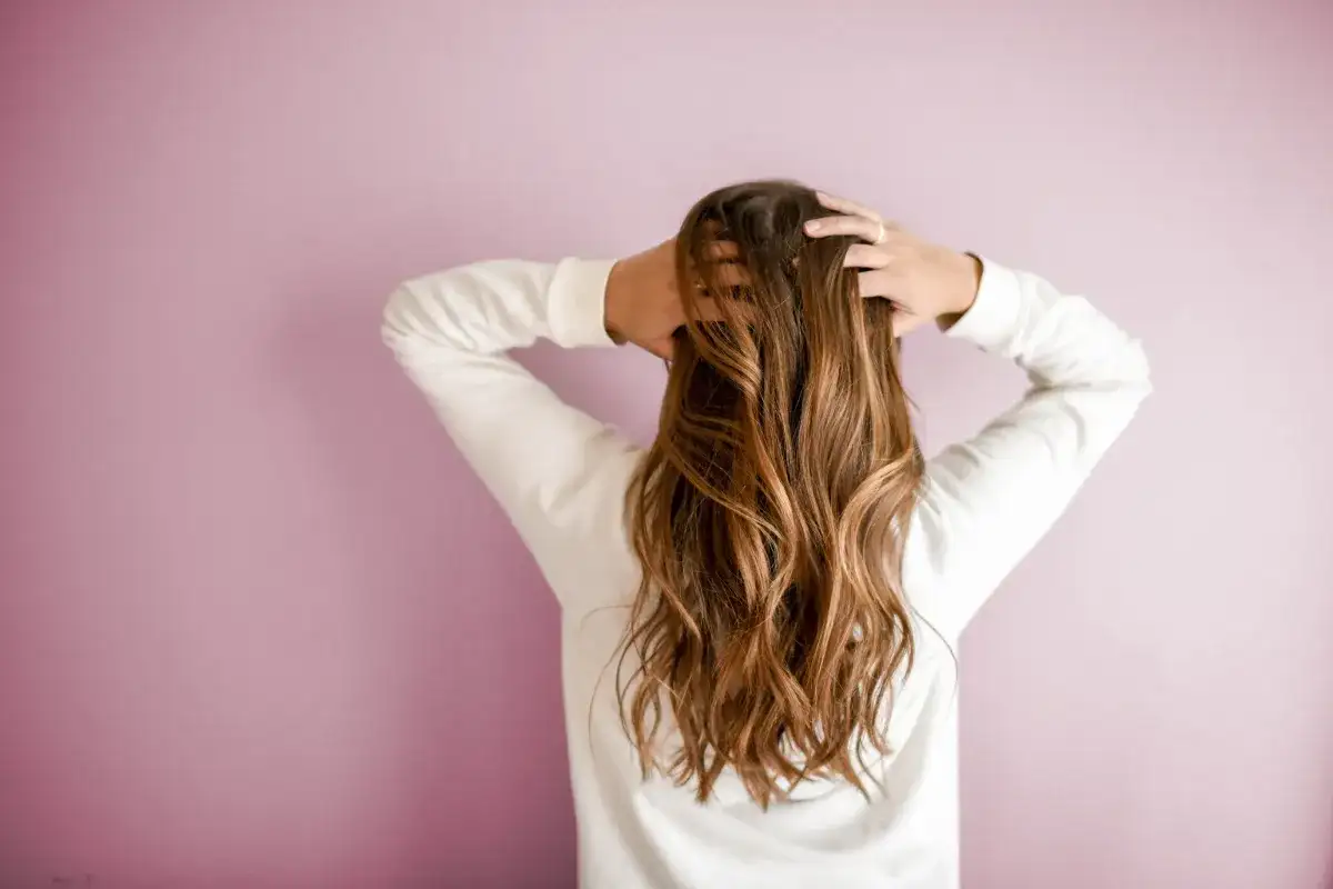 Mujer con cabello castaño ondulado, con mechas matizadas, tocándose la cabeza.