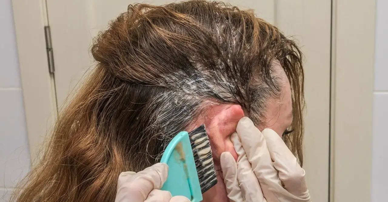 Manos enguantadas aplican tinte en el cabello. Aprende c&oacute;mo quitar manchas de tinte de la piel f&aacute;cilmente.
