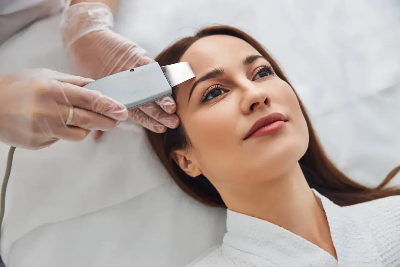 Una cosmetóloga realiza un peeling ultrasónico en la frente de una mujer. Este tratamiento de belleza ayuda a renovar la piel.