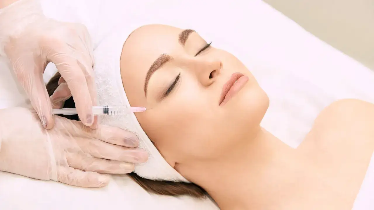 Una mano enguantada aplica una inyección en la mejilla de una mujer, mostrando los beneficios de la mesoterapia para una piel radiante.