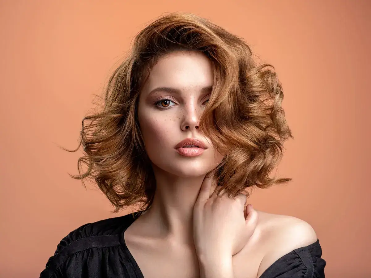 Mujer con cabello casta&ntilde;o ondulado y peinados c&oacute;modos, con un toque de maquillaje y pecas.