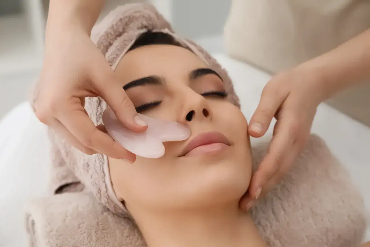 Manos expertas realizan un drenaje linfático facial con una piedra de jade para relajar y revitalizar la piel.