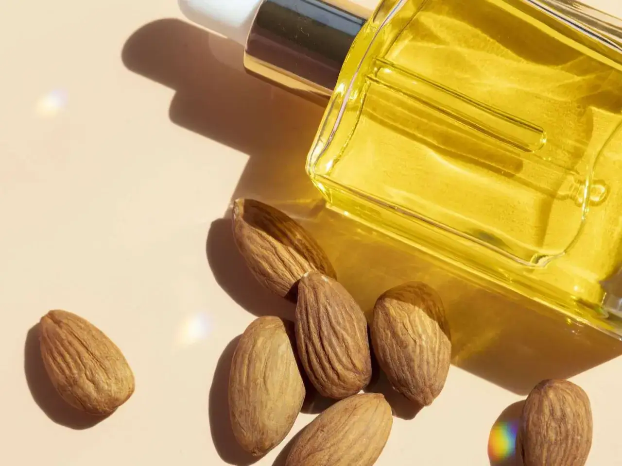 Aceite de almendras en frasco, rodeado de almendras enteras. Considera las desventajas del aceite de almendras antes de usarlo.
