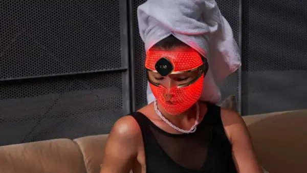 Una mujer con toalla en la cabeza usa una máscara LED facial roja. Descubre para qué sirve esta máscara de belleza.