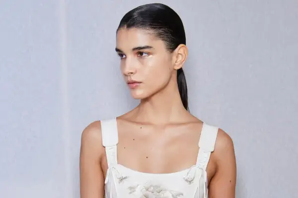 Mujer con coleta alta lisa, maquillaje sutil y vestido blanco bordado.
