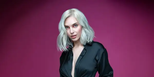 Mujer con cabello rubio platino y ojos azules, vestida con una camisa negra. Aprende como matizar el pelo en casa para lograr este look.