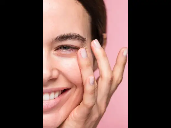 Una mujer sonríe mientras se aplica suavemente un producto en el contorno de ojos. Las opiniones sobre contorno ojos freshly son muy positivas.