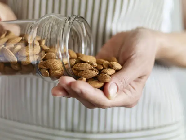Manos sostienen almendras cayendo de un frasco. Considera las desventajas del aceite de almendras antes de usarlo.