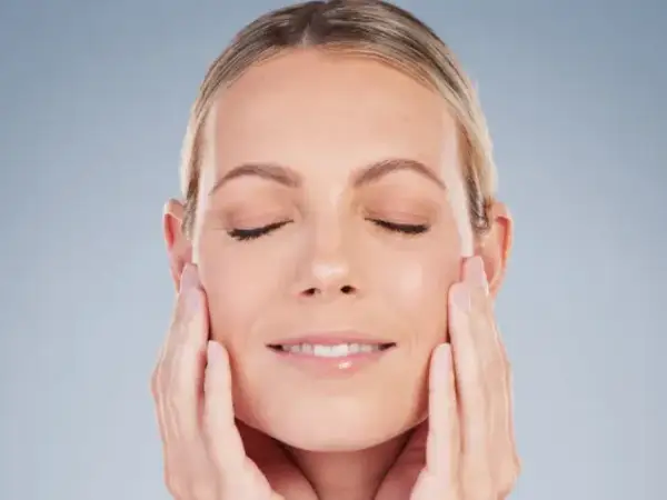 Mujer con ojos cerrados y una sonrisa suave, acariciando su rostro para realzar su óvalo facial.