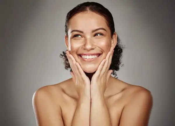 Mujer sonríe con las manos en las mejillas, disfrutando de los efectos de la radiofrecuencia facial para una piel radiante y rejuvenecida.