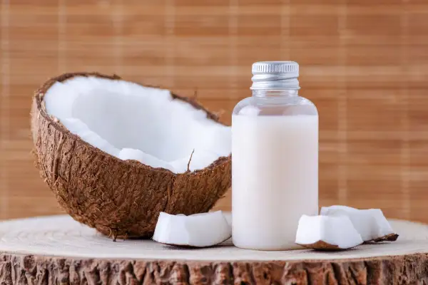 Aceite de coco en botella junto a coco partido. Considera las contraindicaciones del aceite de coco antes de usarlo.