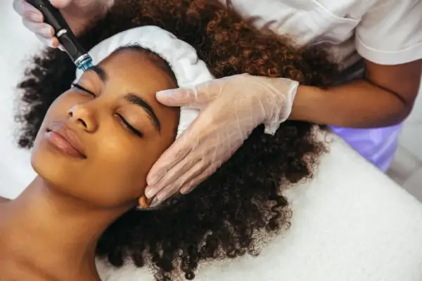 Una mujer disfruta de un tratamiento Hydrafacial. Un profesional con guantes aplica el dispositivo en su rostro para una piel radiante.