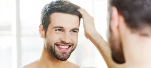 Hombre sonriente se toca el cabello, reflejando su confianza en sus tratamientos de belleza para hombres.