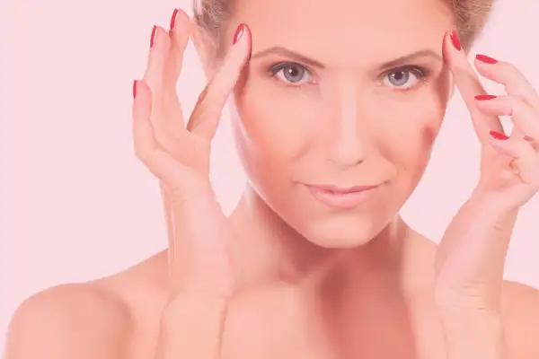 Mujer con manos en la frente, piel radiante tras carboxiterapia facial.