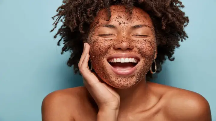 Mujer sonríe con la cara cubierta de un exfoliante, mostrando lo que es exfoliar la piel para una tez radiante.